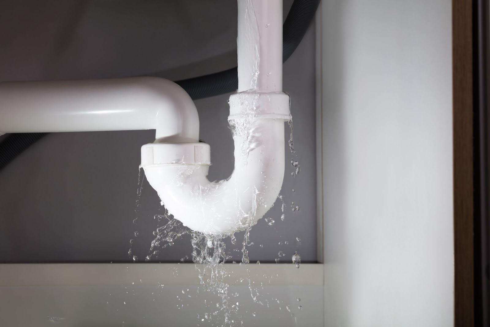Hidden plumbing leak under sink showing water dripping from PVC drain pipe