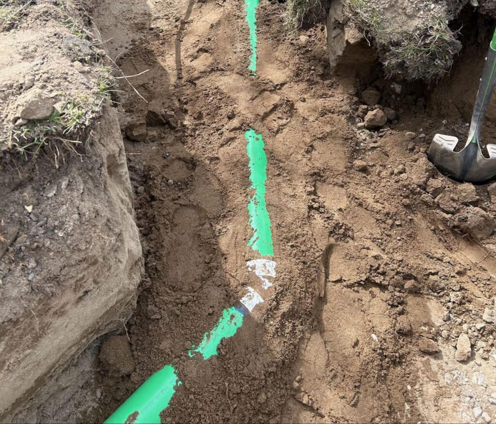 Green sewer line exposed in an open trench during an underground excavation