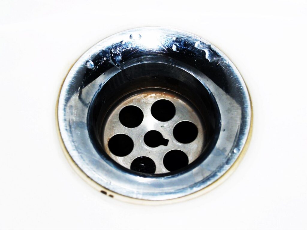 Close-up of a metal sink drain, a common starting point for sewer smells