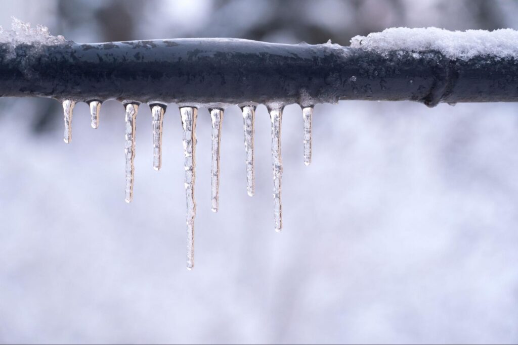 Icicles hanging from an outdoor pipe show why preventing frozen pipes starts in fall
