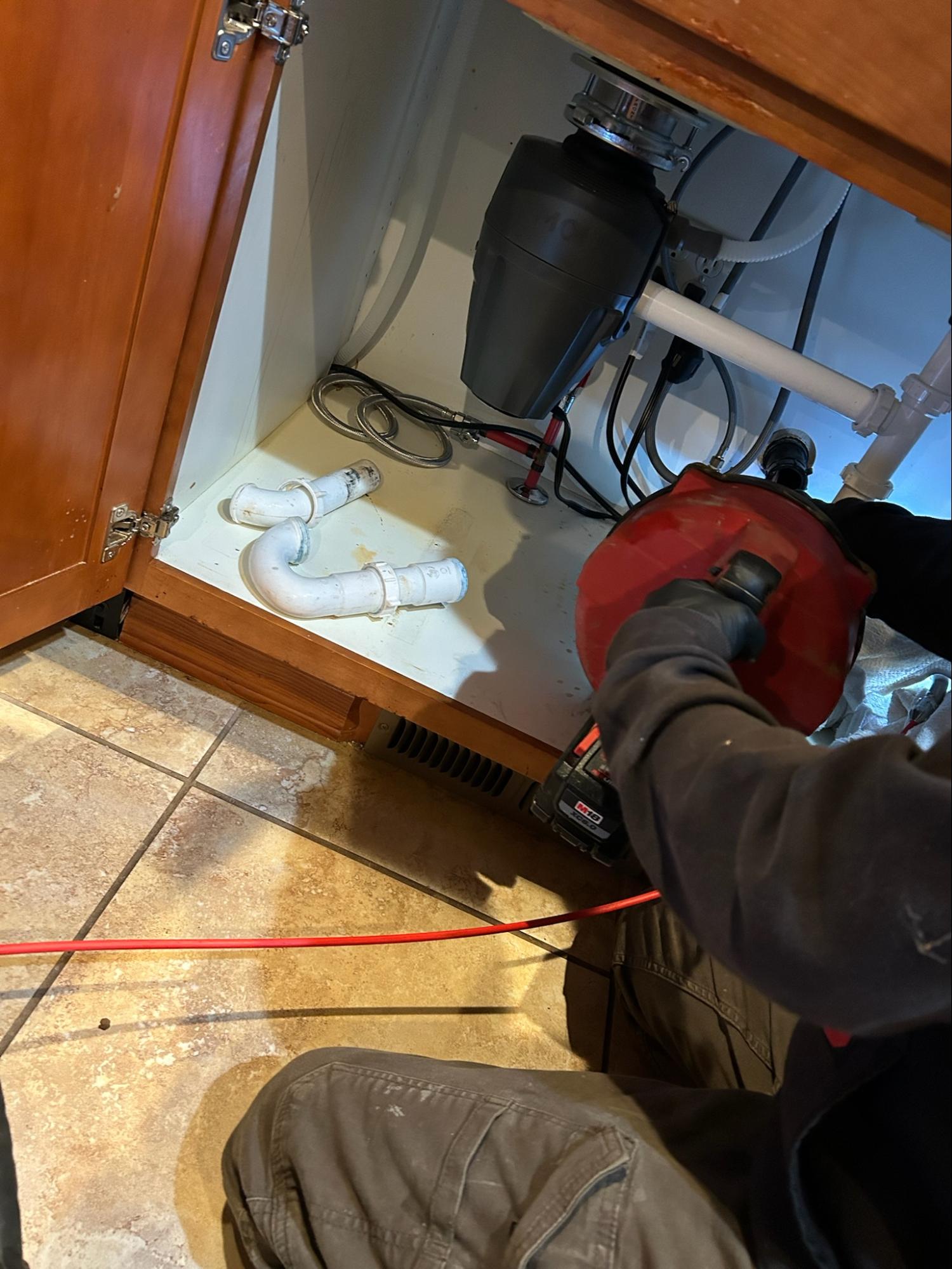 An A&N technician snaking a kitchen sink drain beneath a garbage disposal in East Wenatchee, WA.